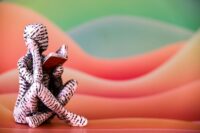 Small sculptural figure reading an open book before a colorful backdrop