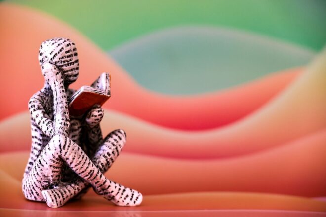 Small sculptural figure reading an open book before a colorful backdrop